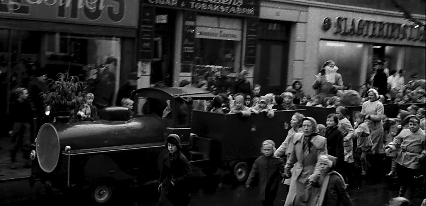 En stor bil med nisser kører forbi butikkerne i hovedgaden - i 1955