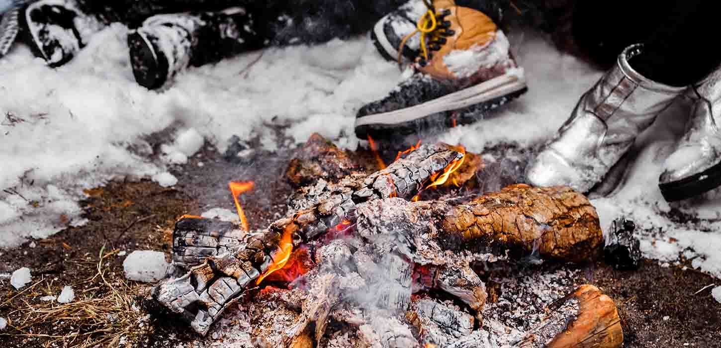 Menschen sitzen in einem verschneiten Winter mit großen Stiefeln am brennenden Feuer