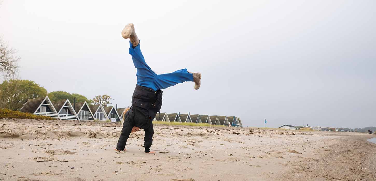 Barn slår vejrmøller på Hasmark Strand i efteråret med sommerhuse i baggrunden