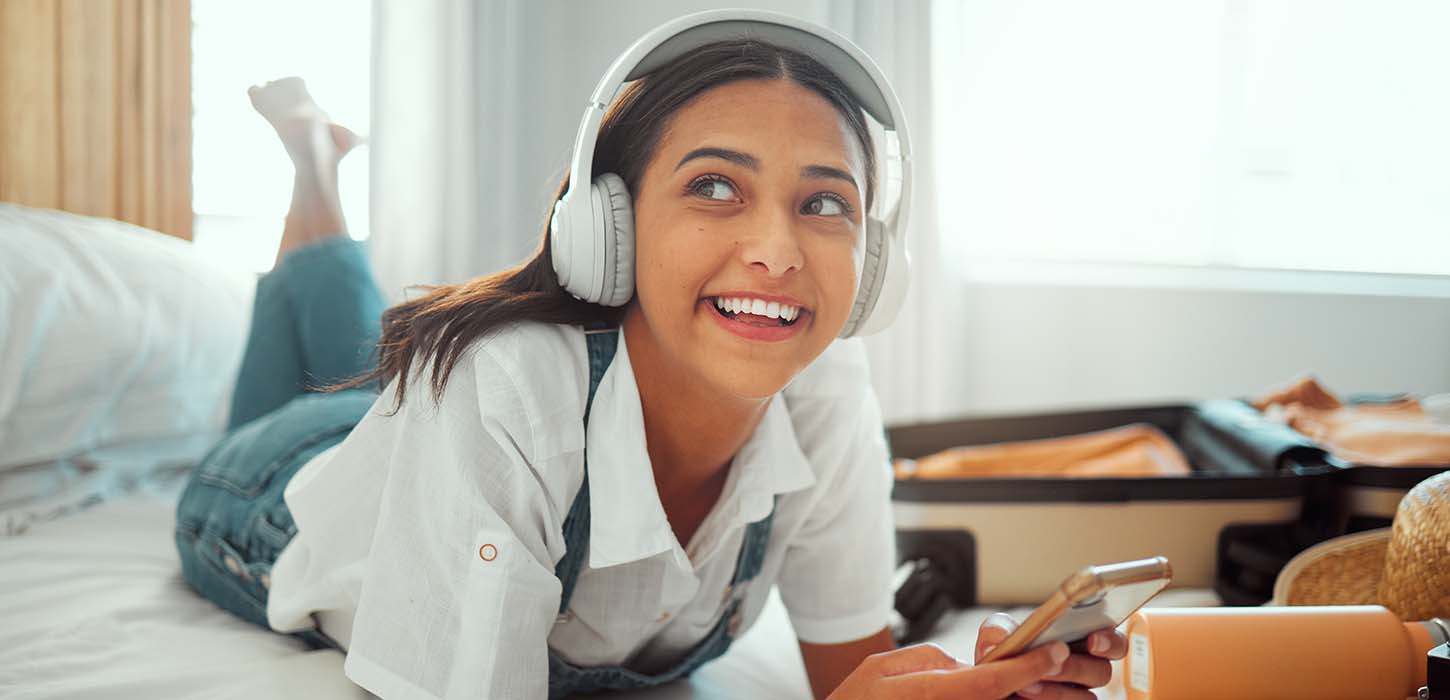 Glad kvinde lytter til musik på hotelseng