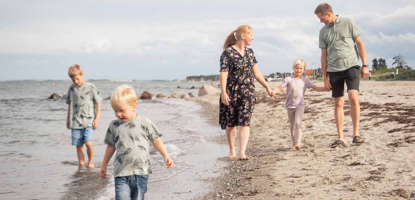 Familie med tre børn går tur på stranden