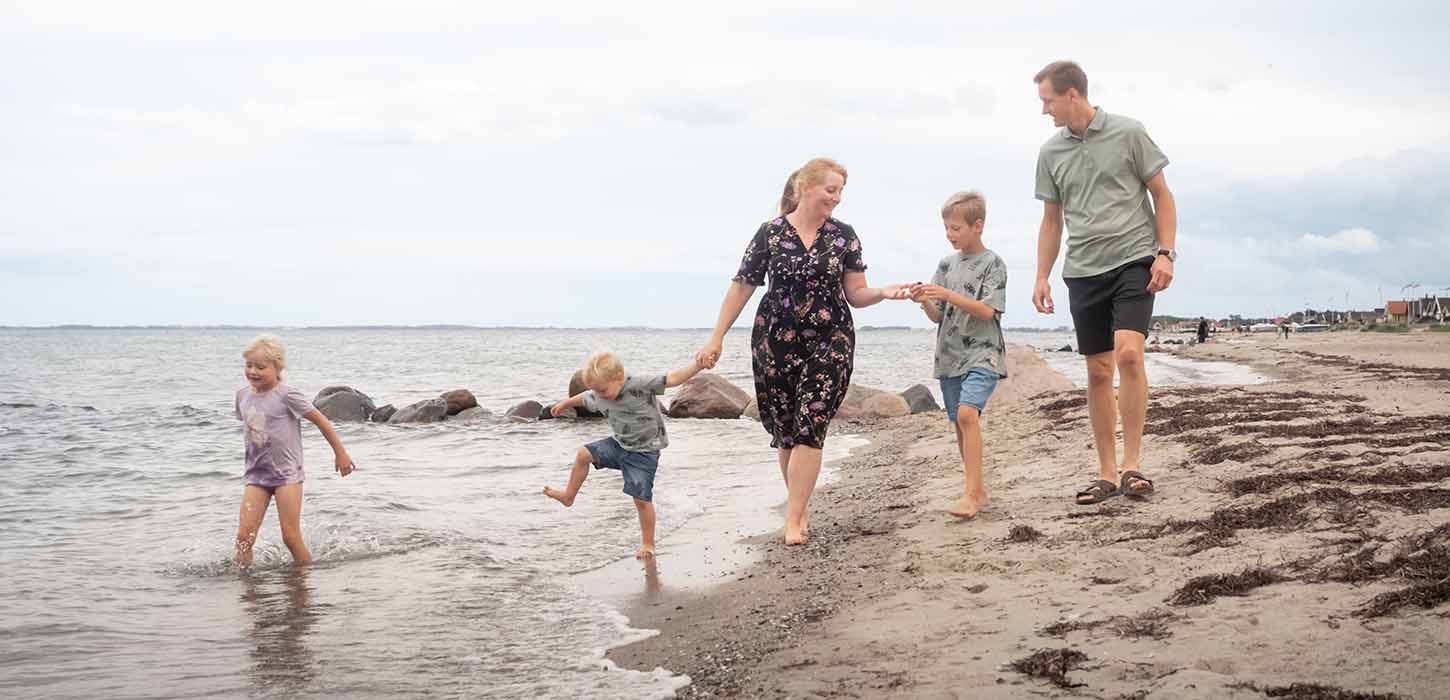 Familie går tur på Hasmark Strand og leger i vandet