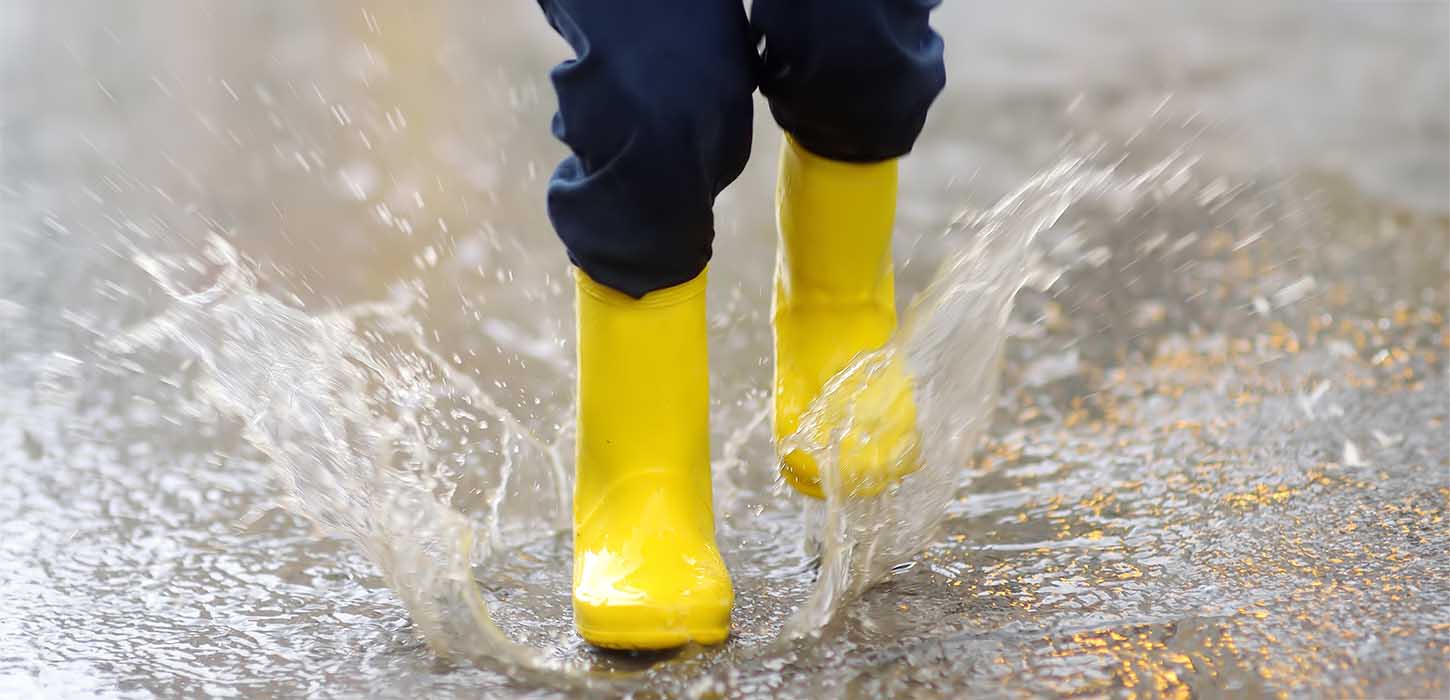 Et barn i gummistøvler hopper i regnvand